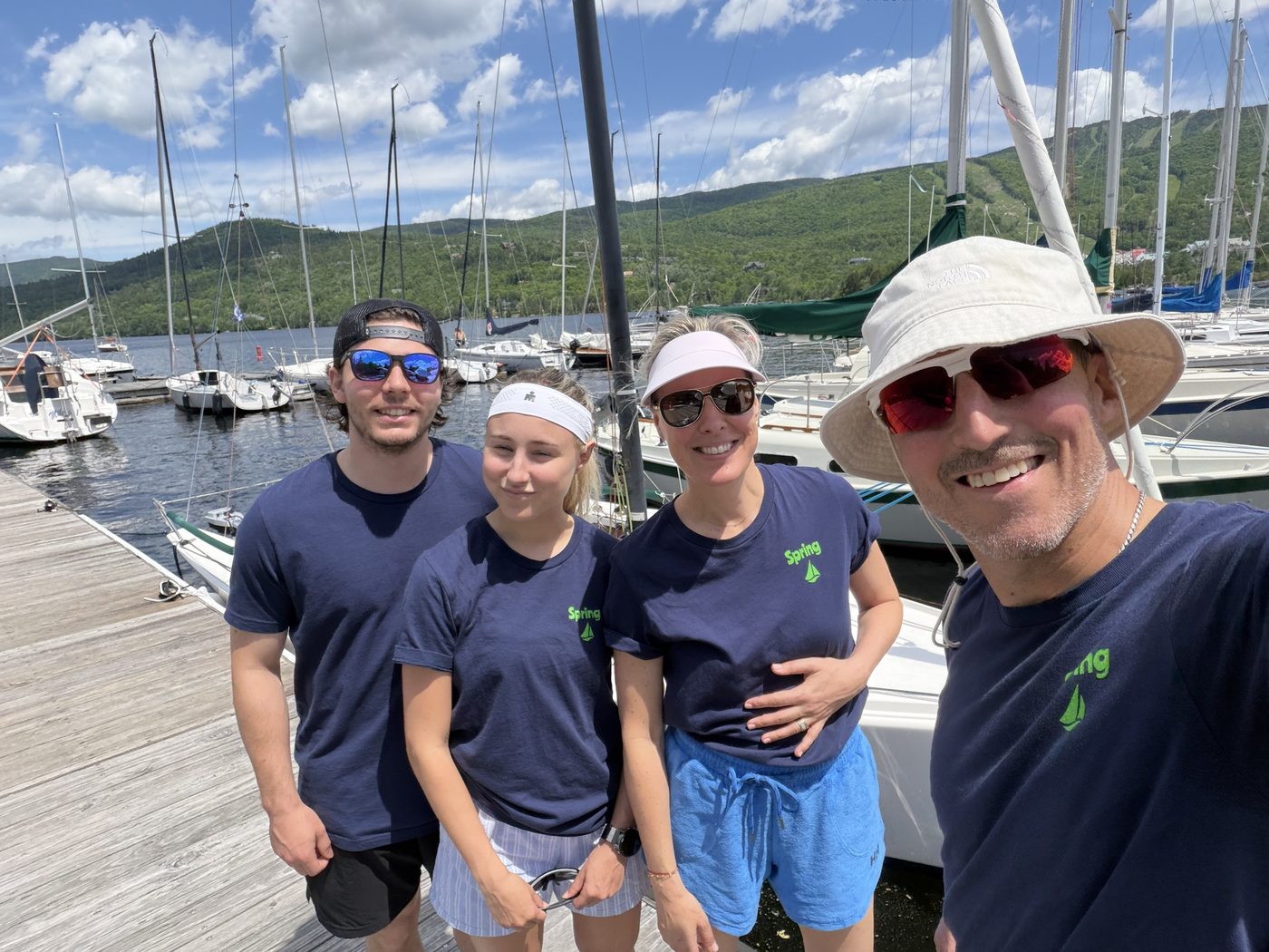 The Spring crew of CAN157 on a pontoon at Lake Tremblant — left to right Ralf, Emma, Tania and Jean-Sébastien Pilon, sailboats and green hills behind.